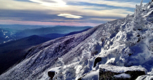 Snow-covered mountain landscape with rugged peaks and a cloudy sky, showcasing a serene winter scene.