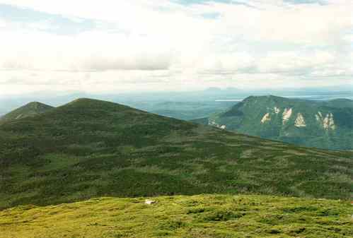 A panoramic view of green mountains under a cloudy sky, showcasing rolling hills and distant peaks.
