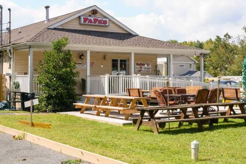 A small restaurant with a patio, picnic tables, and a sign reading "Pappy's" surrounded by greenery and blue skies.