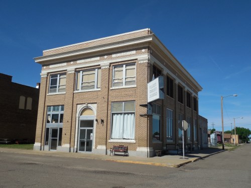 Historic brick building with large windows, a sign, and a bench outside, set against a clear blue sky.