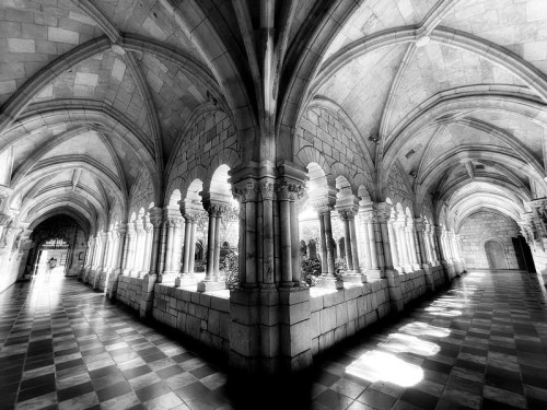 Black and white image of a grand stone corridor with arches and columns, featuring intricate architectural details.