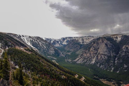A panoramic view of a mountainous landscape with snow-capped peaks and a lush green valley under a cloudy sky.