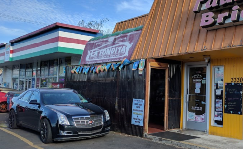 A black car parked outside a colorful restaurant with a sign reading "La Fundita" and a vibrant awning.
