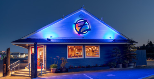 A blue restaurant exterior illuminated with blue lights, featuring a logo and large windows showcasing a cozy interior.