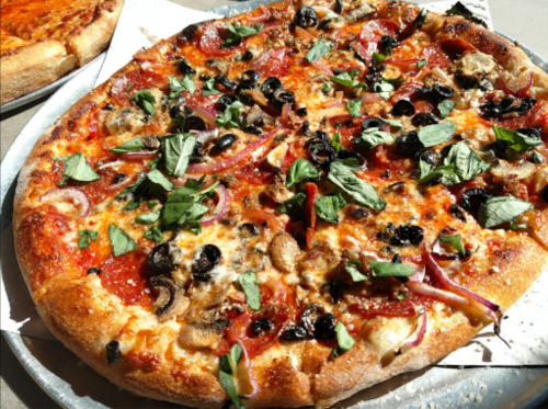 A close-up of a pizza topped with pepperoni, olives, mushrooms, red onions, and fresh basil on a silver tray.