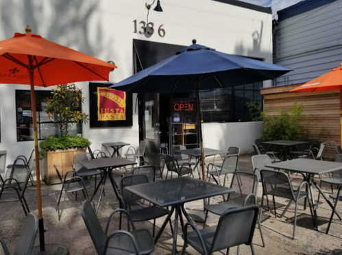 Outdoor dining area with tables and umbrellas in front of a restaurant, featuring an "OPEN" sign.
