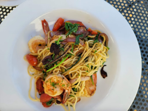 A plate of shrimp pasta with tomatoes, greens, and herbs, served on a white dish.