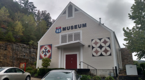 Exterior of the U.S. 23 Museum, featuring quilt patterns on the walls and parked cars in front.