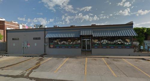 A single-story building with a blue awning and large windows displaying colorful murals, set against a cloudy sky.