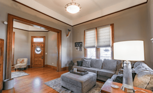 Cozy living room with gray sofa, wooden accents, and a warm light fixture, featuring a door and windows with blinds.