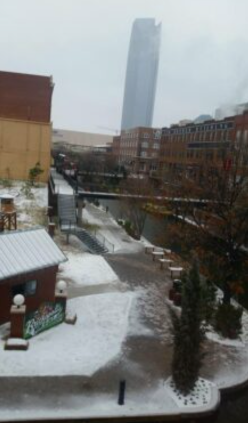 A snowy urban scene featuring buildings, a canal, and a tall skyscraper in the background.