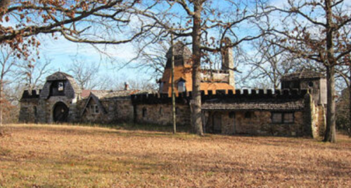 A stone castle with turrets surrounded by trees and fallen leaves under a clear blue sky.