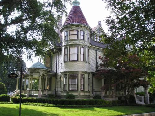 A large, ornate Victorian-style house with a turret, green trim, and a well-maintained garden.