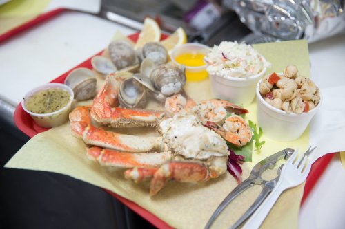 A seafood platter featuring crab legs, shrimp, clams, coleslaw, and a side salad on a red tray.