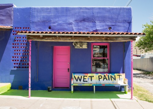 A vibrant purple building with a pink door and a sign reading "Wet Paint" on a colorful bench outside.