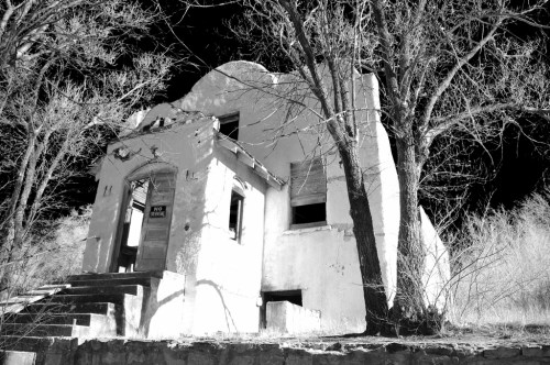 A dilapidated white house with a staircase, surrounded by bare trees, captured in black and white.