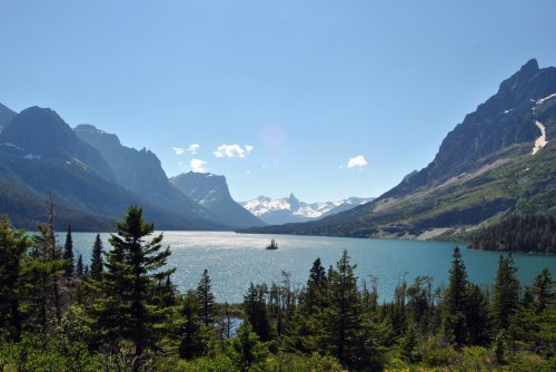 A serene lake surrounded by mountains and lush trees under a clear blue sky.
