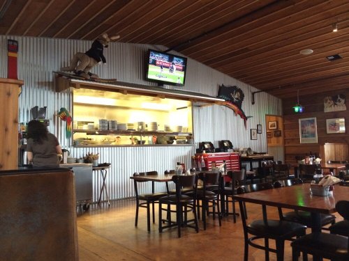 Interior of a rustic restaurant with wooden decor, an open kitchen, and a TV showing a sports game.
