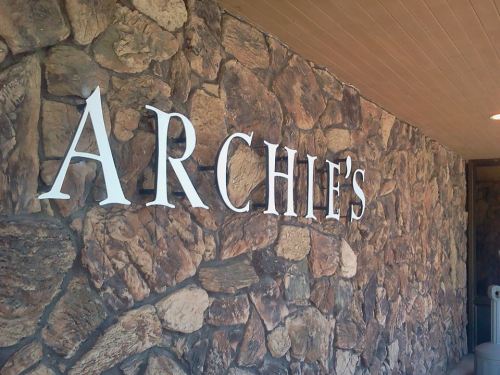 Sign reading "Archie's" on a stone wall.
