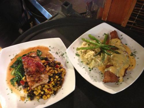 Two plates of food: one with grilled fish on a bed of corn and spinach, the other with fried fish and creamy sauce.