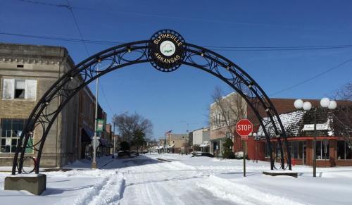 Snow-covered street in Blytheville, Arkansas, featuring an archway sign and a stop sign under a clear blue sky.