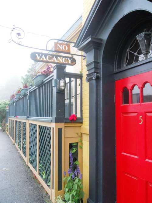 A red door with a "No Vacancy" sign, surrounded by a decorative fence and plants, in a foggy setting.