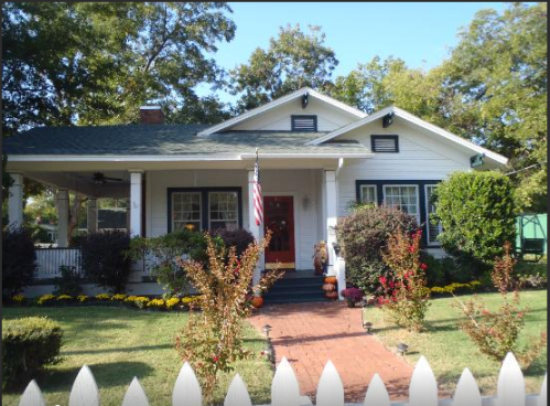 A charming white house with a green roof, surrounded by colorful flowers and a white picket fence.