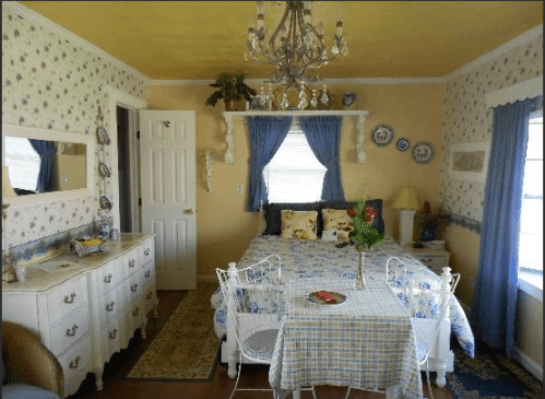 Cozy bedroom with floral wallpaper, a chandelier, a double bed, and a small dining table by the window.