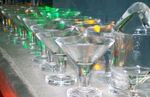 A row of empty martini glasses on a bar, illuminated by colorful lights.