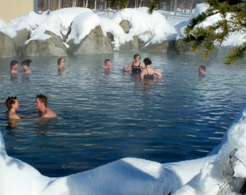 People enjoying a hot spring surrounded by snow-covered rocks and trees on a winter day.