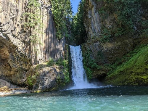 A serene waterfall cascades down rocky cliffs, surrounded by lush greenery and a clear blue pool below.