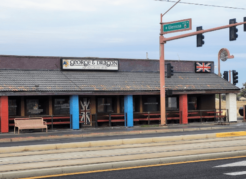 Exterior of "George & Dragon," an English pub, featuring a British flag and colorful benches under a cloudy sky.