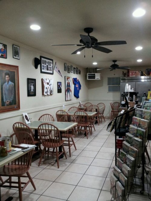 A cozy restaurant interior with wooden chairs, tables, wall art, and a magazine rack. Brightly lit and inviting atmosphere.