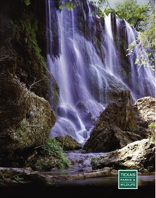 A serene waterfall cascades over rocky cliffs, surrounded by lush greenery in a tranquil natural setting.