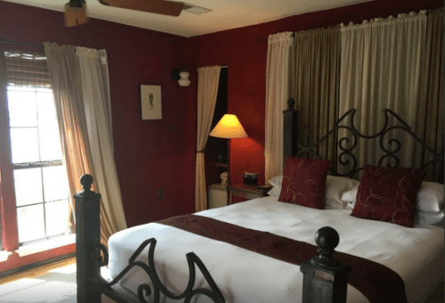 Cozy bedroom with a red accent wall, a large bed, decorative pillows, and soft lighting from a lamp.