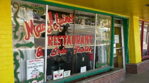 Colorful storefront of MacAlpine's Restaurant & Soda Fountain, featuring large windows and a bright yellow awning.