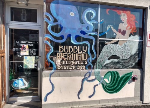 Colorful mural of an octopus and a mermaid on a bar window, promoting "Bubbly Mermaid Champagne & Oyster Bar."