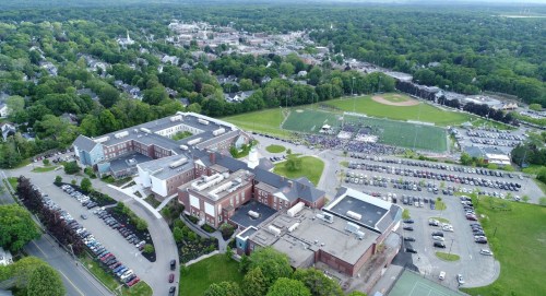 Aerial view of a school campus with sports fields, parking lots, and surrounding greenery in a suburban area.