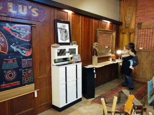 A cozy interior featuring wooden walls, art pieces, and a woman holding a child, exploring the space.
