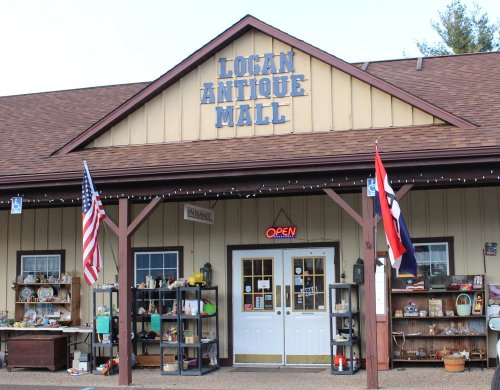 Exterior of Logan Antique Mall with an "Open" sign, featuring flags and displays of antiques outside.