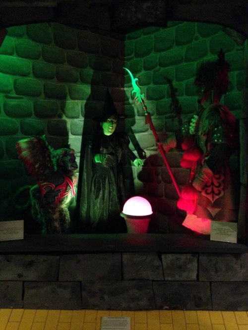 A witch with a green face stands in a stone chamber, flanked by a colorful soldier and a glowing orb.