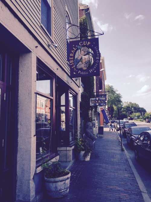 A street view featuring a café sign and a bookstore, with brick pavement and greenery in the background.