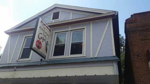 A blue and white building with a sign for a café hanging from the awning. Windows are visible on the upper floor.