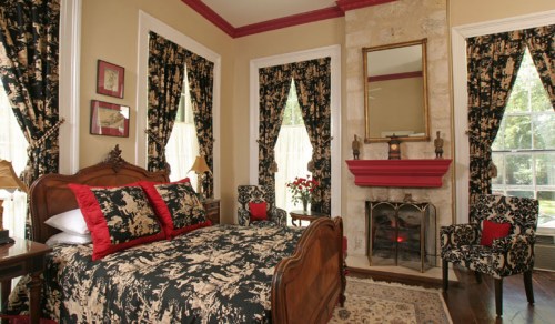 Cozy bedroom with a floral-patterned bedspread, elegant curtains, and a fireplace, featuring warm colors and classic decor.