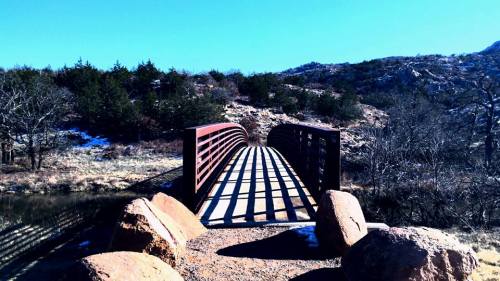 A metal bridge spans a rocky landscape, casting long shadows on the ground under a clear blue sky.