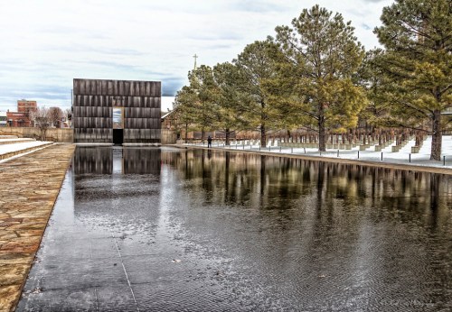 A serene landscape featuring a reflective pool, trees, and a modern building in a peaceful outdoor setting.