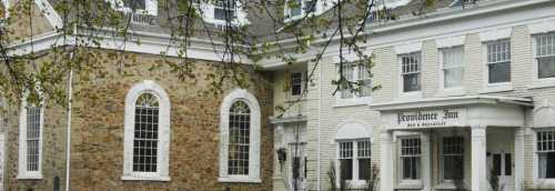 Historic building with stone and white siding, featuring large windows and a sign for "Providence Inn."