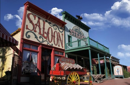 Colorful Western-style buildings, including a saloon and a steakhouse, under a blue sky with fluffy clouds.