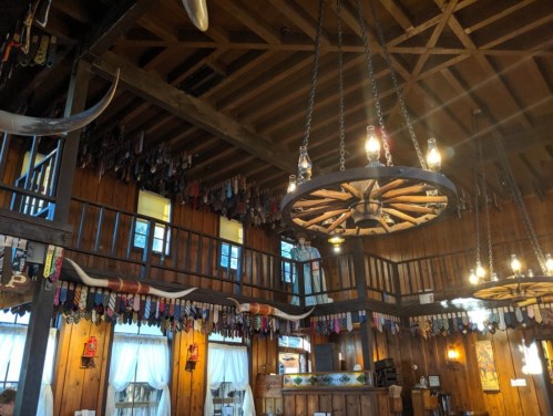 Interior of a rustic restaurant with wooden beams, hanging lights, and colorful ties displayed on the walls.