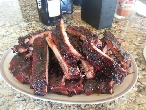 A platter of smoky, glazed barbecue ribs stacked high on a countertop.